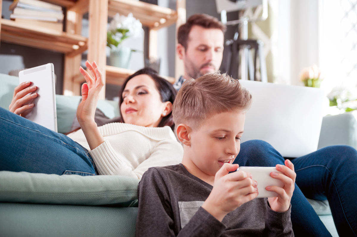 A mom, dad, and son playing on their own devices in a living room