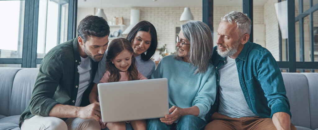 Happy multi-generation family using laptop and smiling while spending time home together