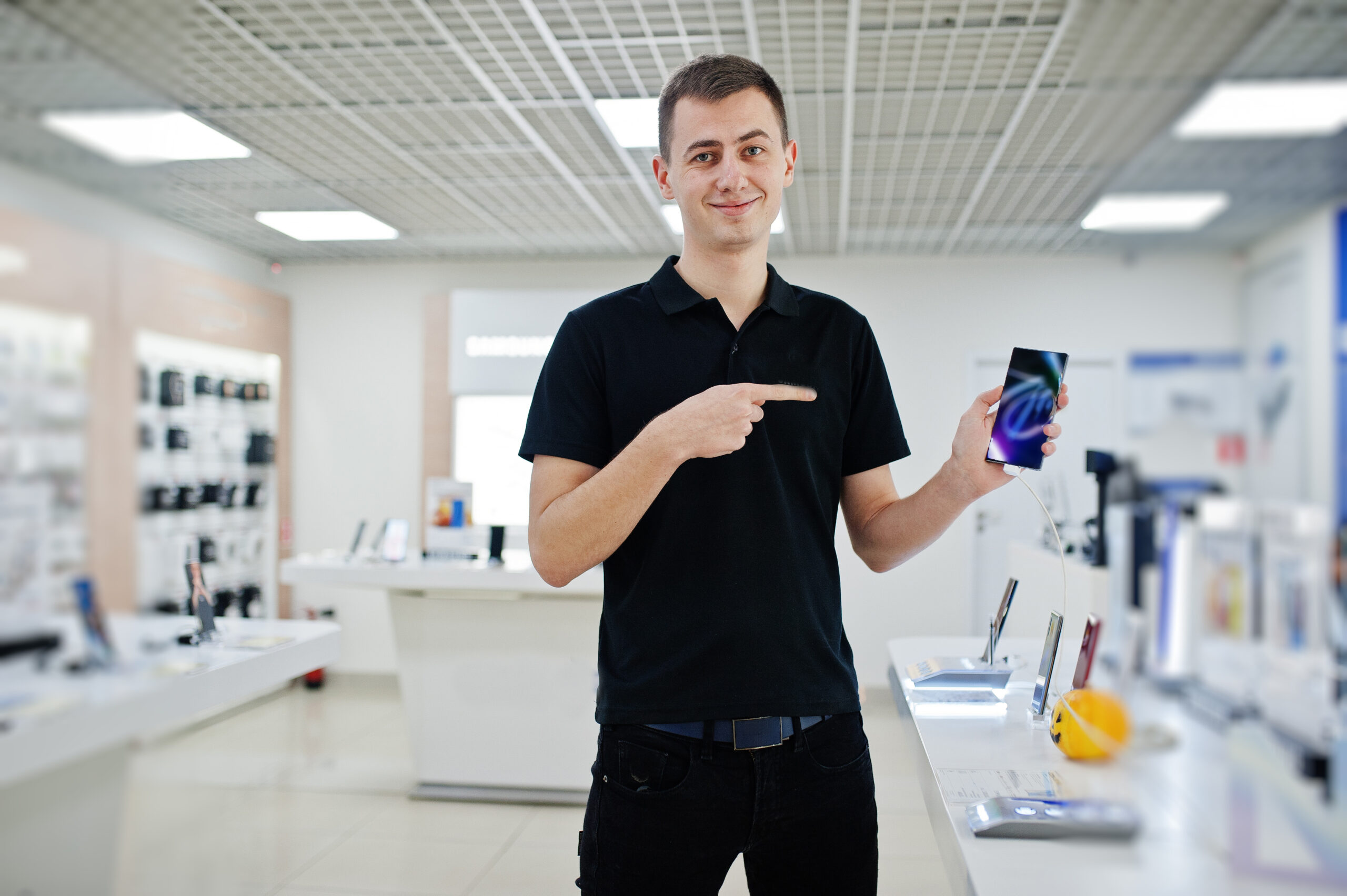 Seller man mobile phone professional consultant in tech store or shop hold new smartphone at  hand and show finger to the screen.